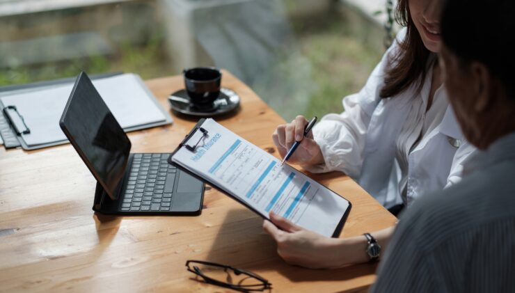 Insurance agent assisting a client with a health insurance application form at a desk